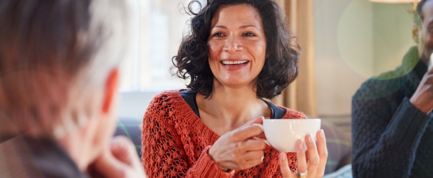 A woman talking to a man while drinking tea.