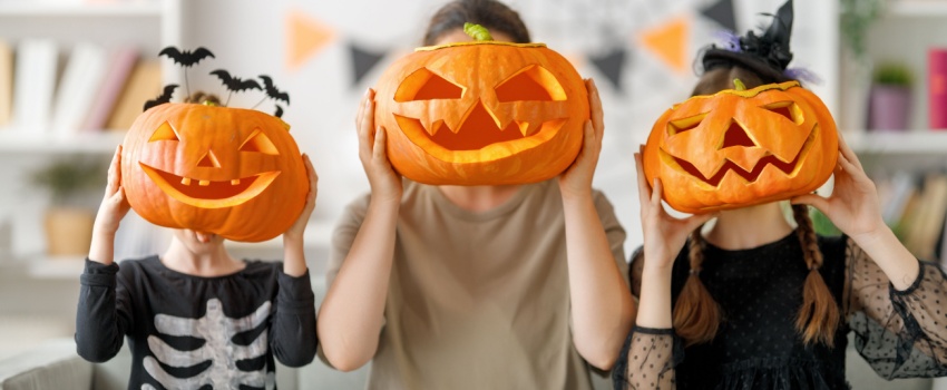 A mother and two children holding up carved pumpkins to their faces.